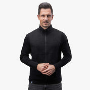 Merino Weste Herren 270 g/m2: Mann in schwarzer Wollweste mit Reißverschluss, ideal als Midlayer für Outdoor-Aktivitäten, bietet Komfort und Funktionalität.