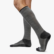 Person trägt Hohe Merino Ski Socken Herren & Damen, die idealen Komfort und Leistung für Skitouren bieten, aus Merinowolle für Wärmeregulierung und Geruchskontrolle.