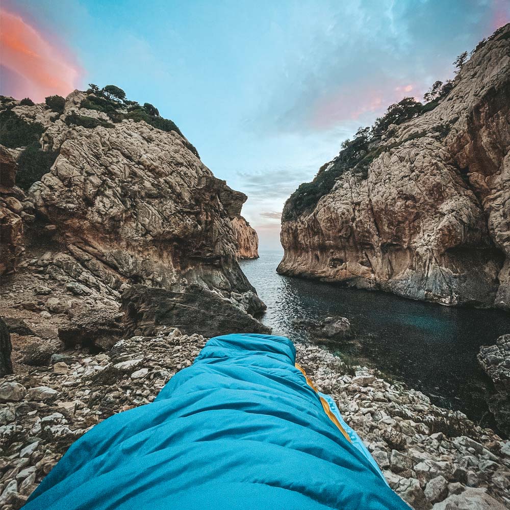 Leichter Sommer Daunenschlafsack auf steinigem Strand, ideal für Outdoor-Abenteuer, kompakt und ultraleicht, passend für Camping und Reisen.