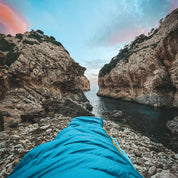 Leichter Sommer Daunenschlafsack auf steinigem Strand, ideal für Outdoor-Abenteuer, kompakt und ultraleicht, passend für Camping und Reisen.