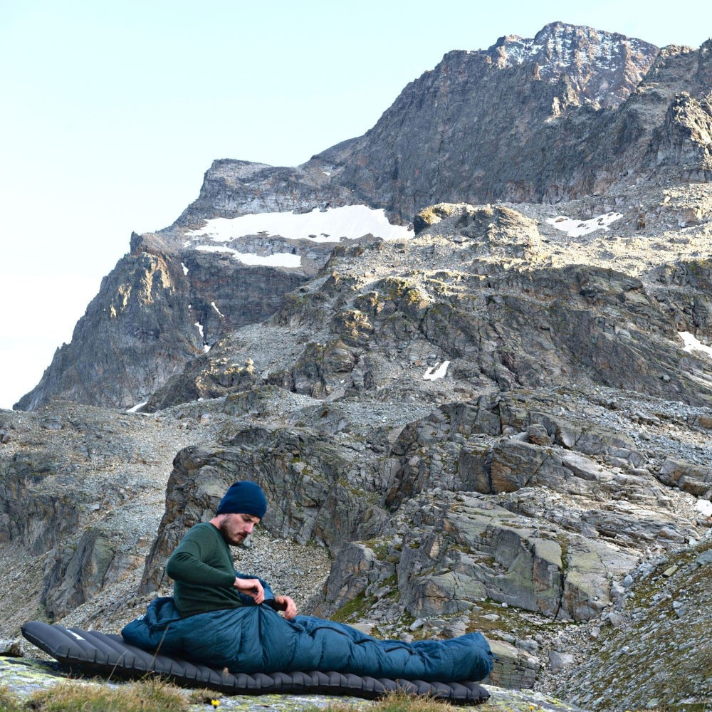Mann in einem 3-Jahreszeiten Schlafsack auf einem Berg, Teil des Alpin Loacker Outdoor-Schlaf-Sets für kühle Nächte und komfortable Outdoor-Erlebnisse.
