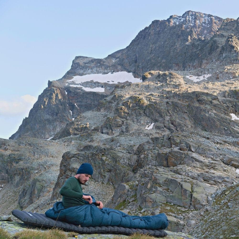 Ein Mann sitzt in einer leichten Isomatte isoliert mit Kunstdaune - 750g, ideal für Outdoor-Aktivitäten wie Camping und Trekking, in felsiger Landschaft.