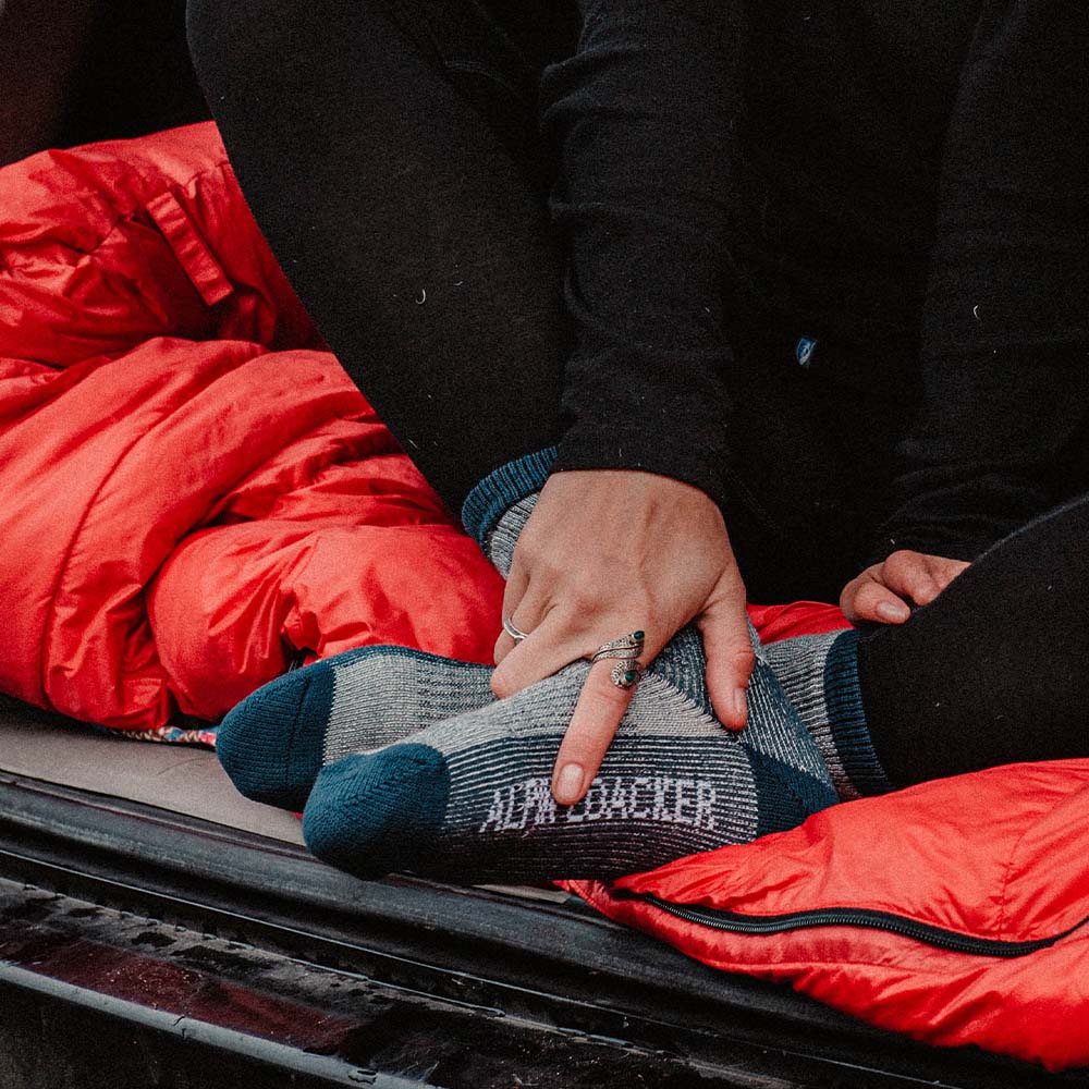 Merino Wandersocken Classic Herren & Damen: Füße in einem roten Schlafsack, betont die Sockenstruktur. Ideal für Outdoor-Abenteuer, atmungsaktiv und temperaturregulierend.