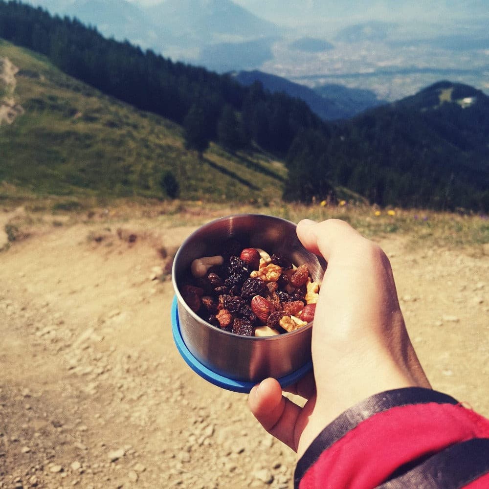 Hand hält Edelstahl Behälter mit Nüssen und Trockenfrüchten, ideal für Outdoor-Abenteuer. Robuste, leichte Lösung für plastikfreie Aufbewahrung von Snacks.