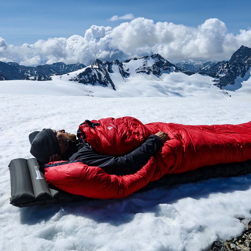 Mann schläft auf Schnee in einem Schlafsack, demonstriert die Leichte Isomatte isoliert mit Kunstdaune - 750g für optimalen Komfort und Isolierung beim Outdoor-Camping.