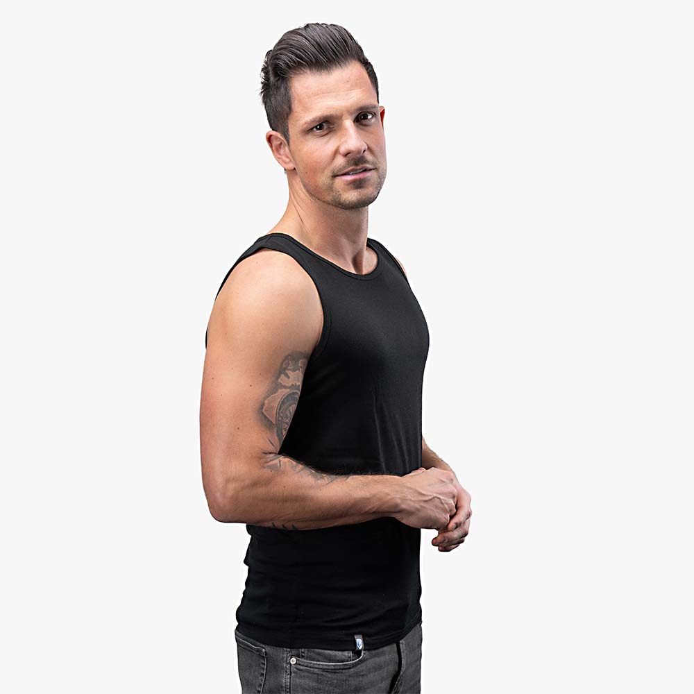 Mann im Merino Tank Top Herren 150 g/m2 von Alpin Loacker, ideal für Outdoor-Aktivitäten, kombiniert Merinowolle mit CORESPUN-Technologie für Komfort und Strapazierfähigkeit.