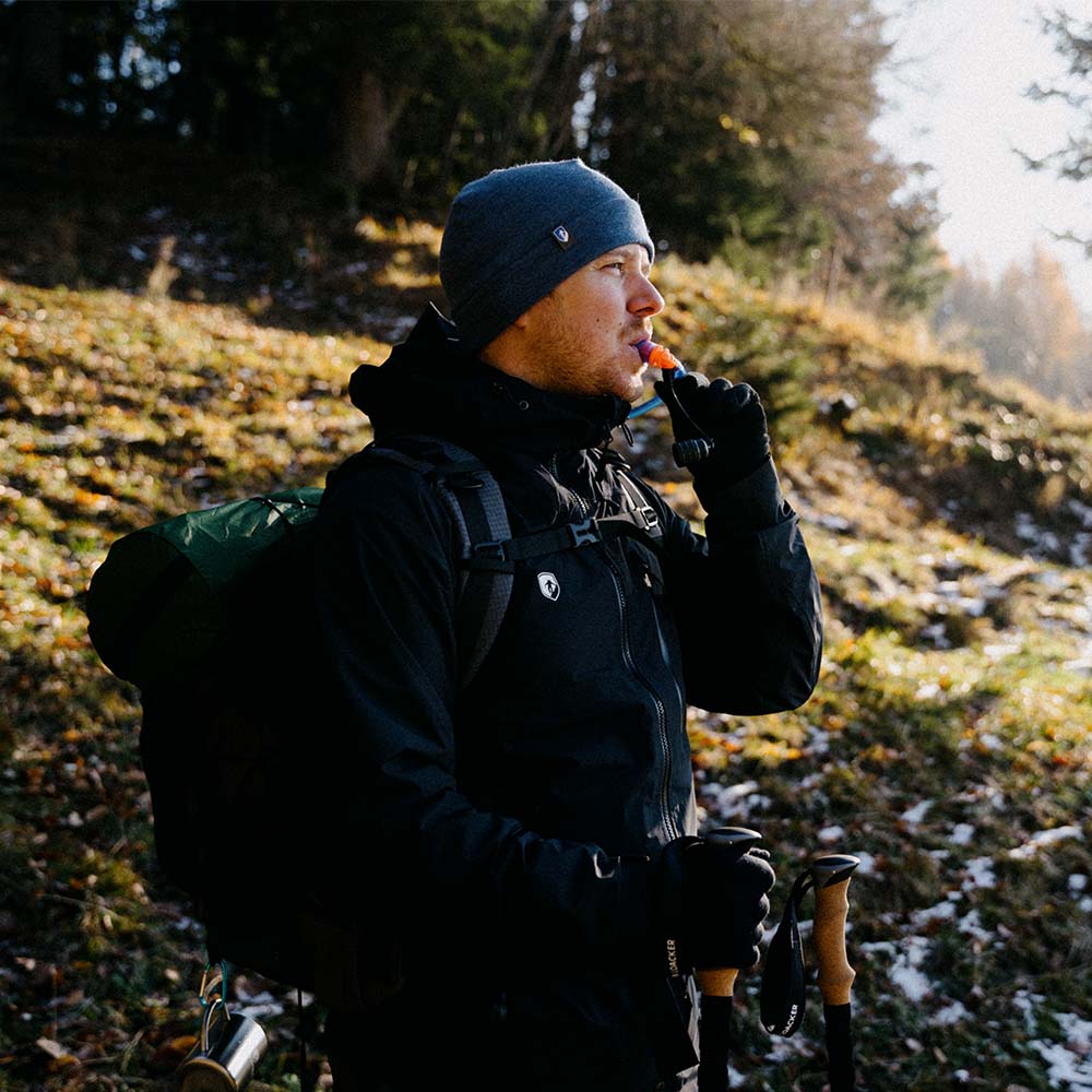 Mann mit Rucksack und Wanderstock, der die ultraleichte Trinkblase für Sommer + Winter von Alpin Loacker für Outdoor-Aktivitäten präsentiert.