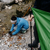 Person mit grünem Tarp 500 auf Felsen, ideal für Outdoor-Abenteuer. Leicht, vielseitig einsetzbar, bietet Schutz vor Regen und Sonne. Perfekt für Trekking und Camping.